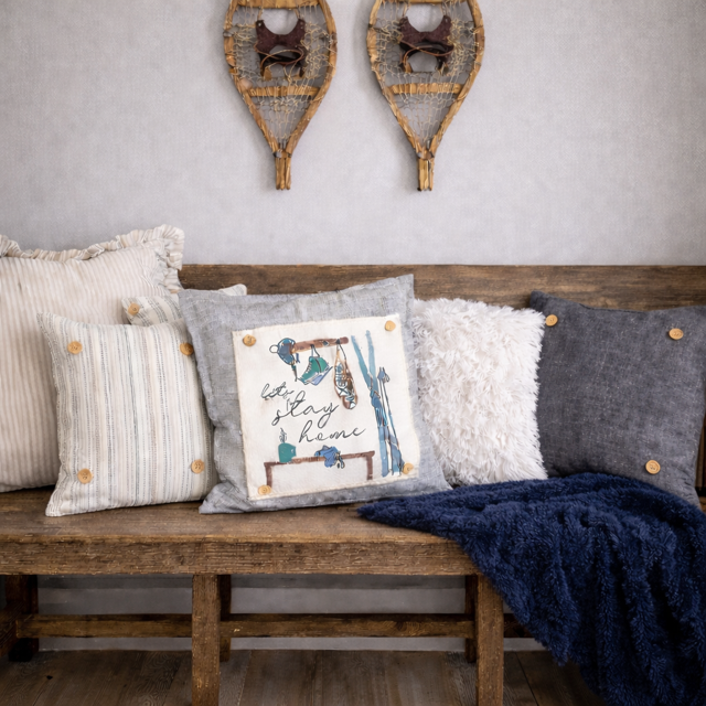 Wooden bench with decorative pillows and a blanket, wall art in the background