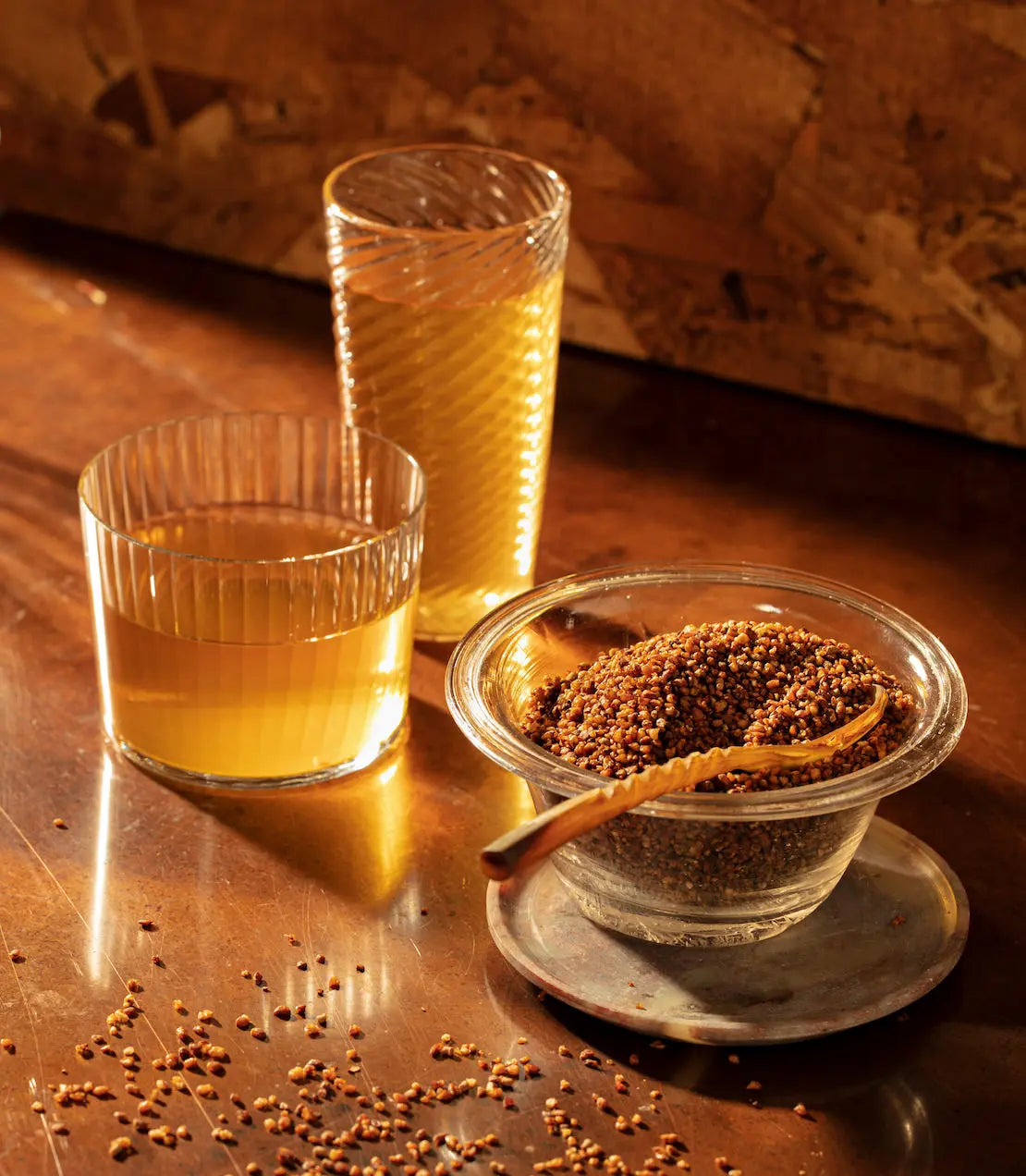 Two glasses of mustard seed oil and a bowl of mustard seeds on a wooden surface.