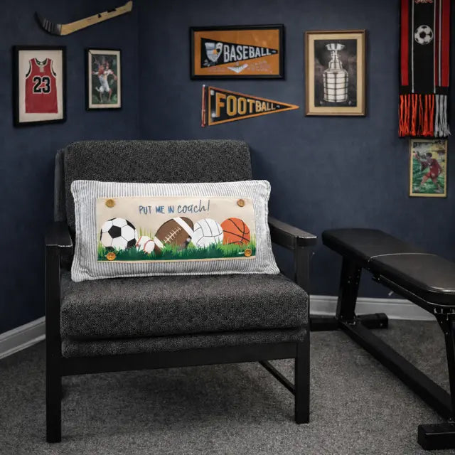 Gray armchair with a decorative pillow featuring sports balls in a room with sports-themed decor.