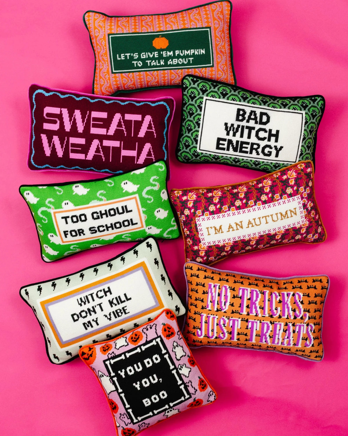 Six decorative embroidered throw pillows arranged on a bright pink background, each with a different Halloween-themed phrase and colorful patterned fabric.