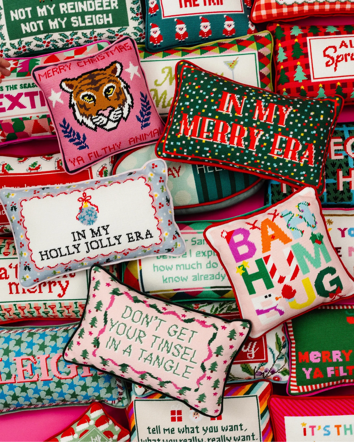 A dense, styled flat-lay collection of various Christmas-themed decorative throw pillows with colorful embroidered patterns and festive text.