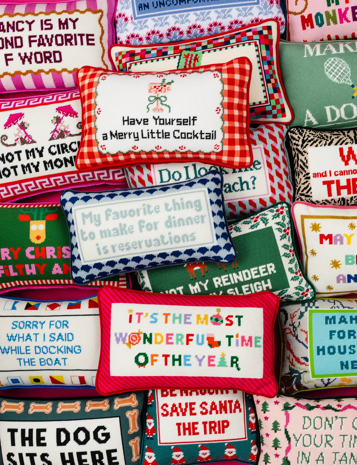 A close-up, stacked arrangement of colorful embroidered decorative pillows with various holiday-themed phrases and patterns.