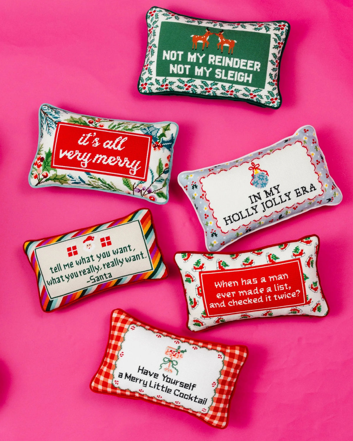Six decorative Christmas throw pillows arranged on a bright pink background, each with a different holiday-themed embroidered design and text.