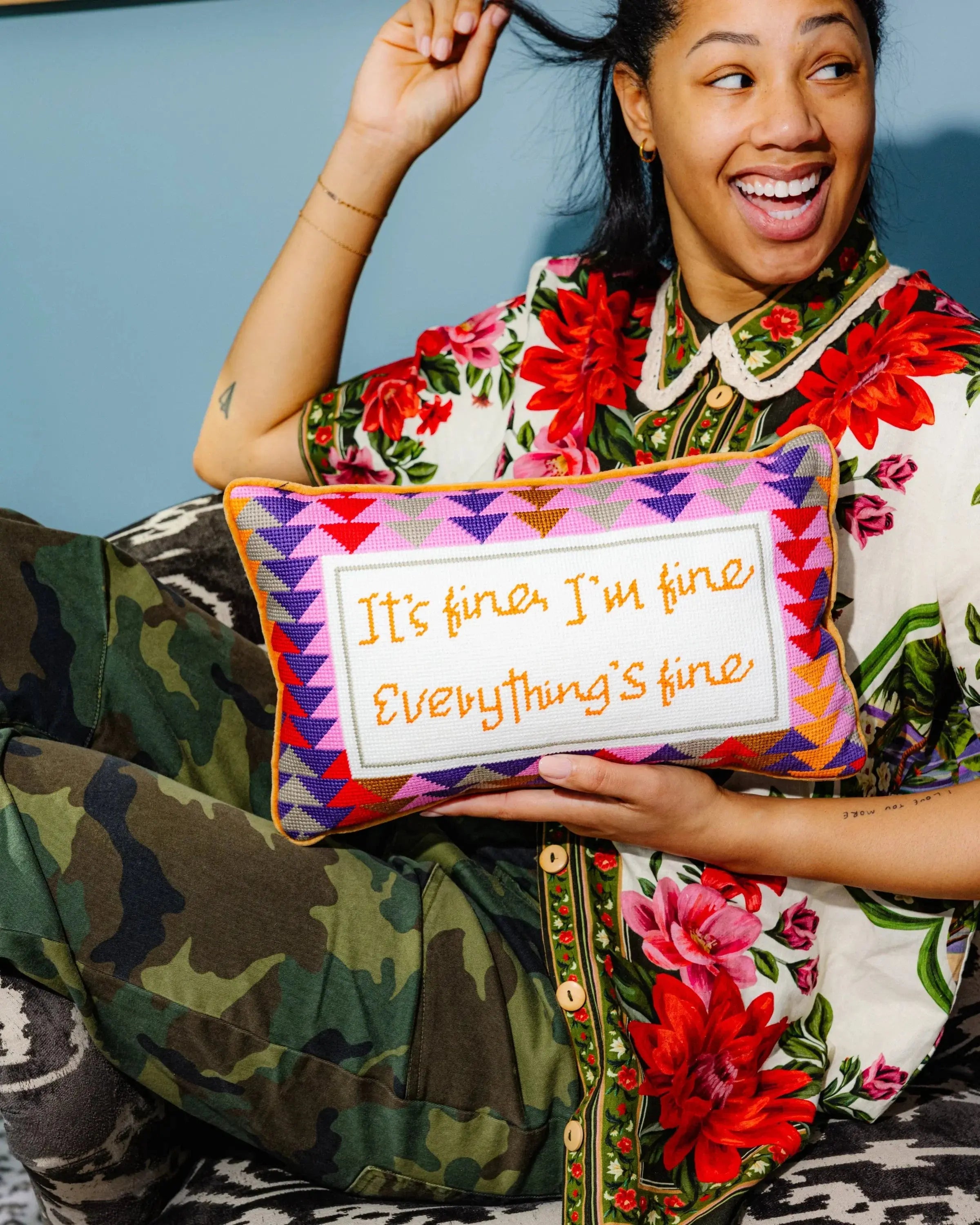 Person holding a pillow with text 'It's fine, I'm fine Everything's fine' against a blue wall.