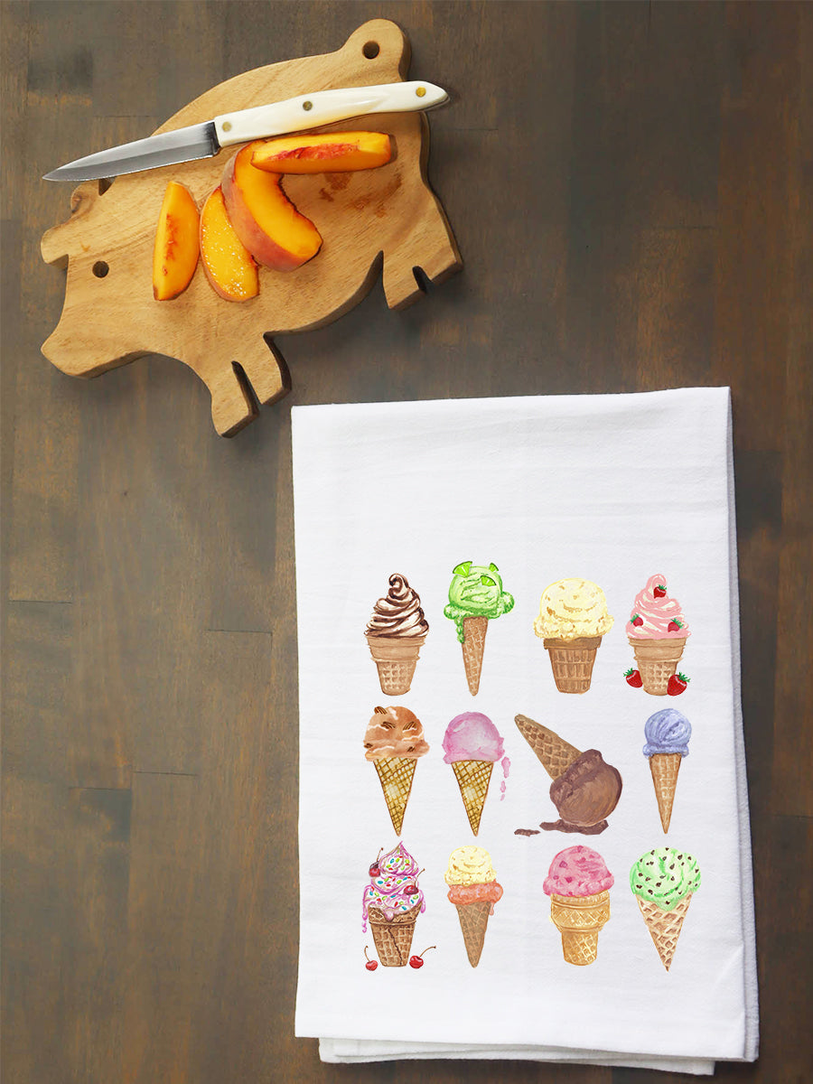 A white kitchen tea towel printed with a grid of colorful ice cream cone illustrations, laid flat on a dark wooden surface next to a wooden cutting board with a knife and peach slices.
