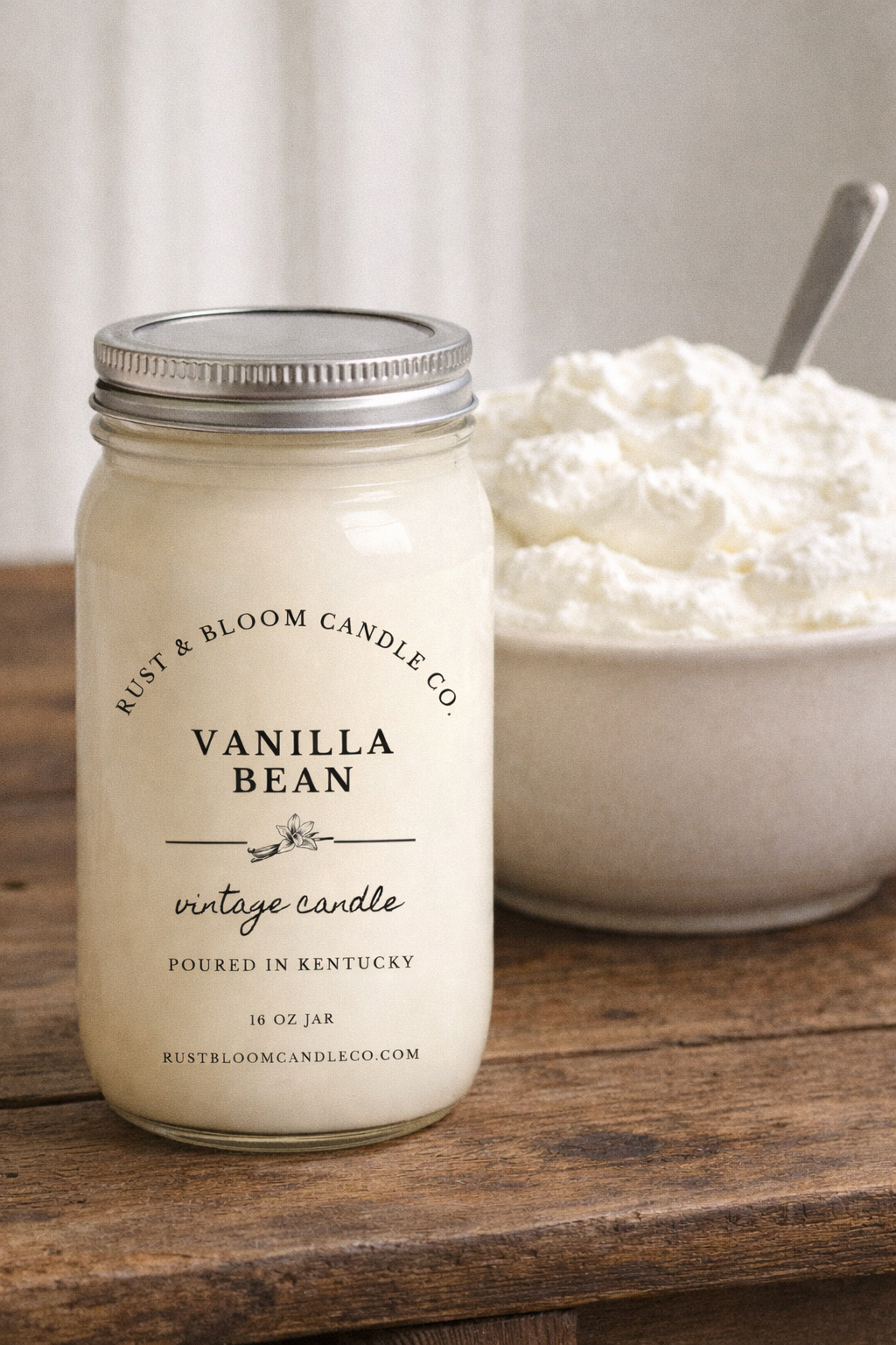 Vanilla bean candle from Rust & Bloom Candle Co. on a wooden surface with a bowl of whipped cream in the background.
