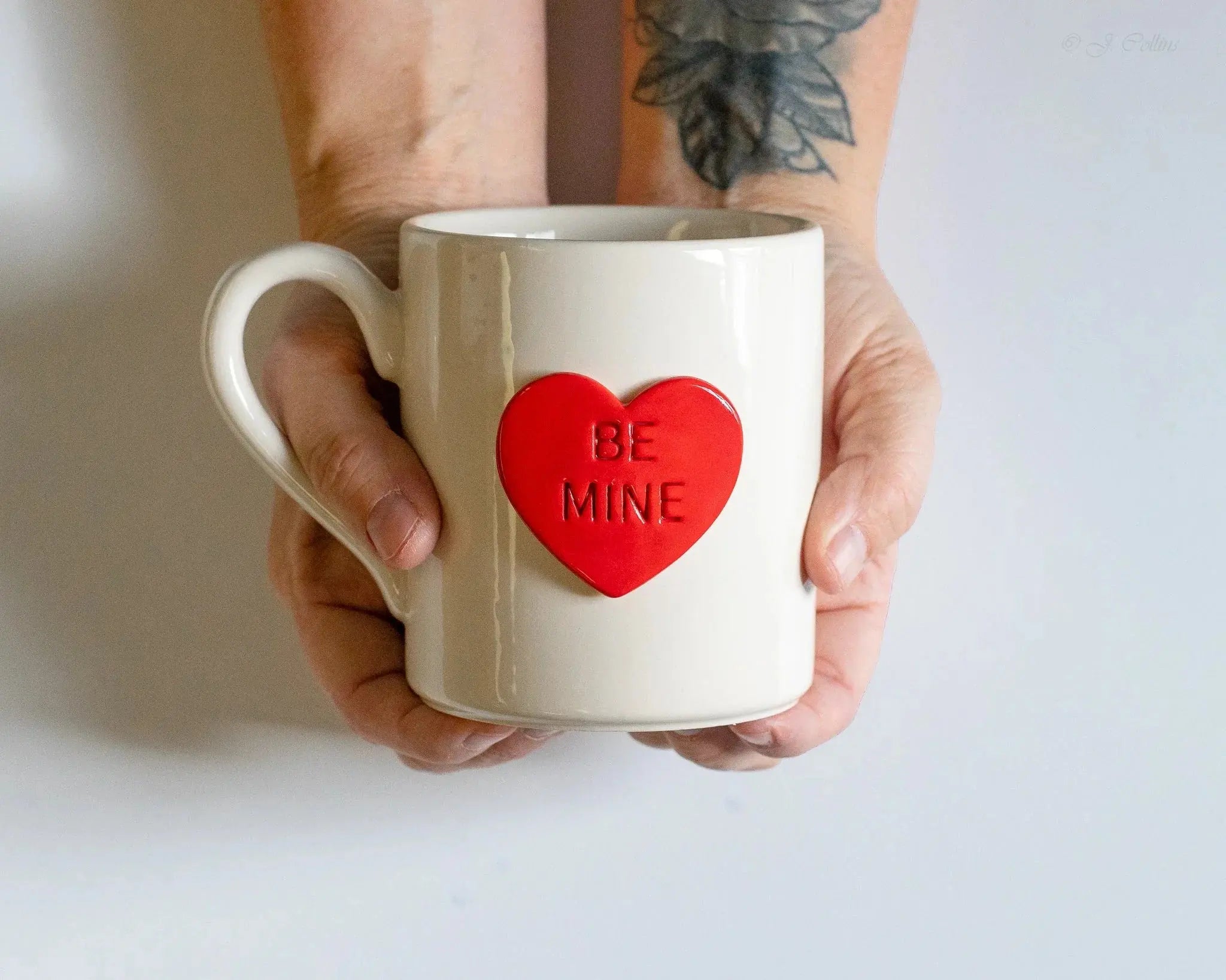 White ceramic mug with red heart saying 'Be Mine', held in hands, cozy farmhouse decor