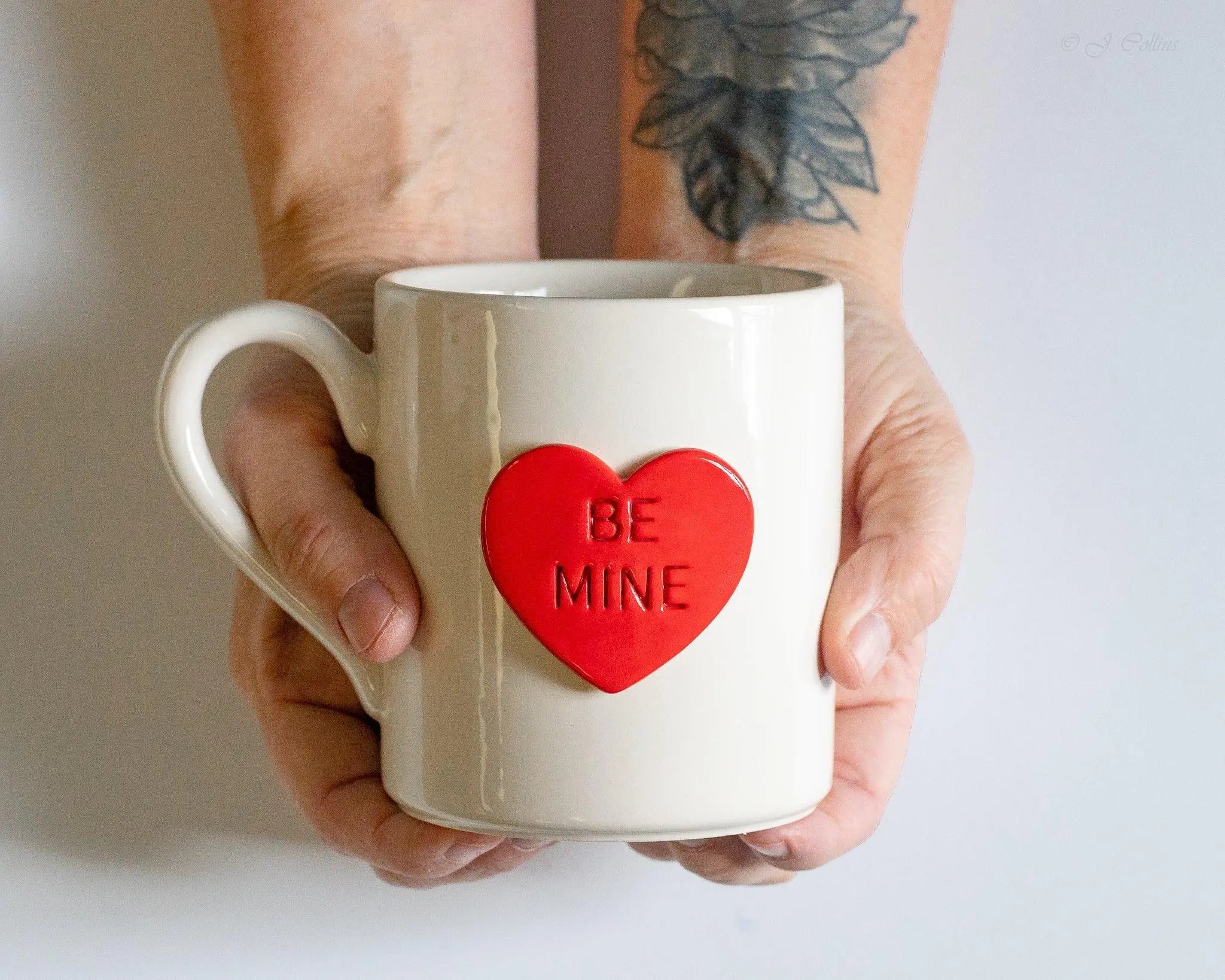 White ceramic mug with red heart saying 'BE MINE', held in hands, cozy farmhouse decor