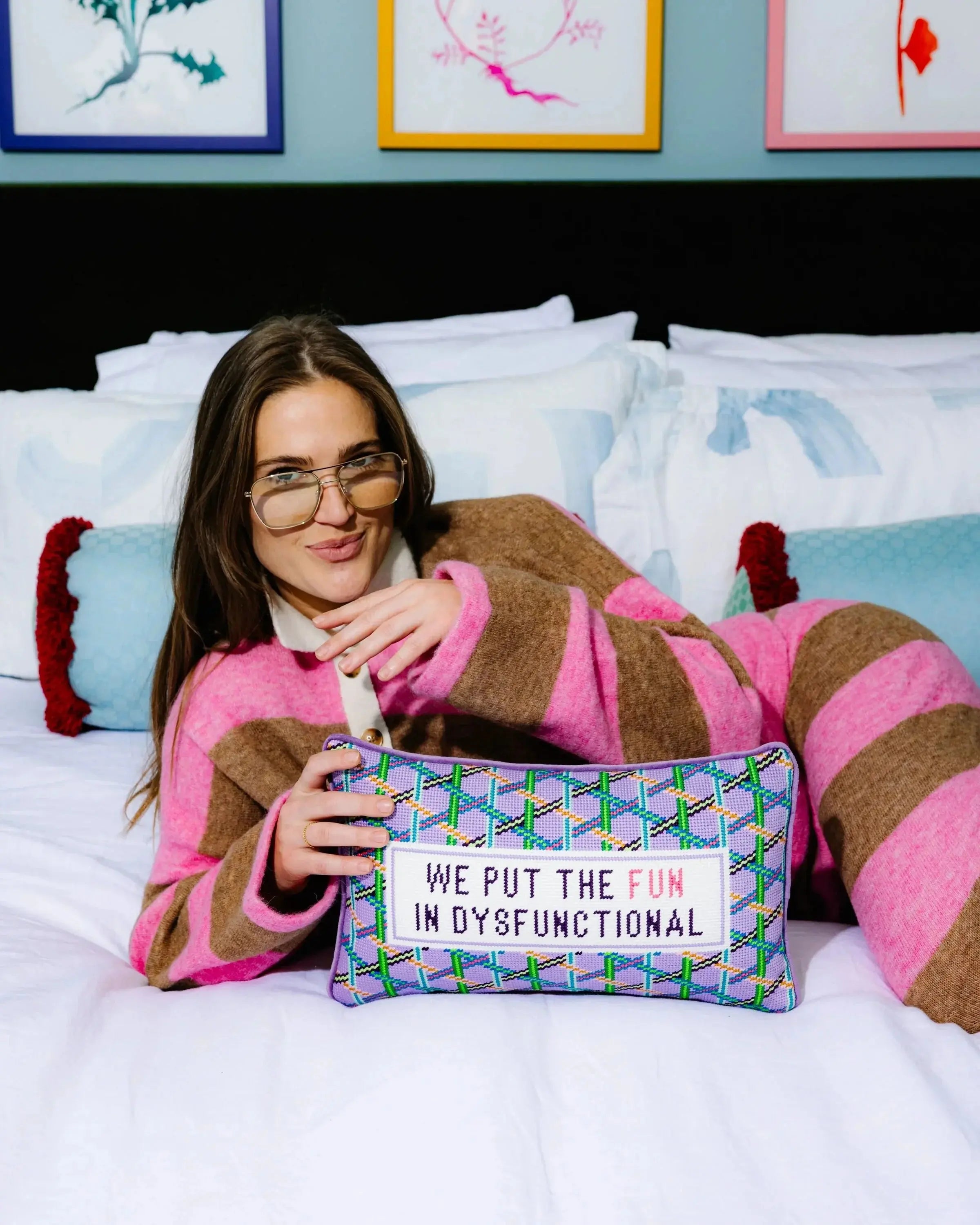 Woman holding a pillow with text on it, sitting on a bed with colorful pillows.