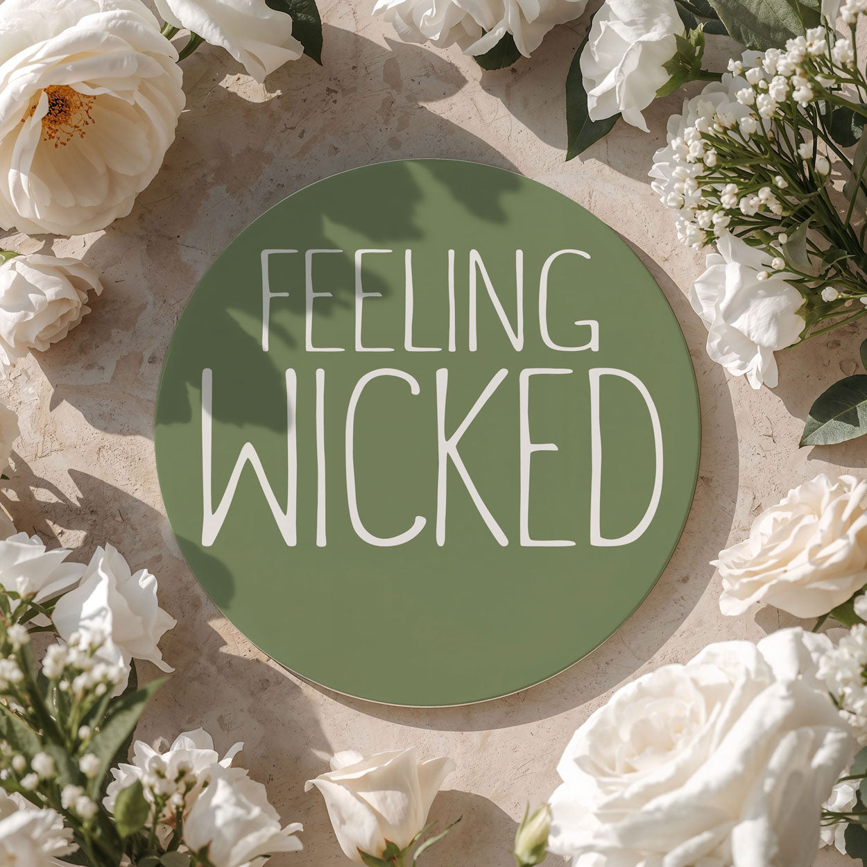 Circular sign with 'FEELING WICKED' text surrounded by white flowers on a beige background