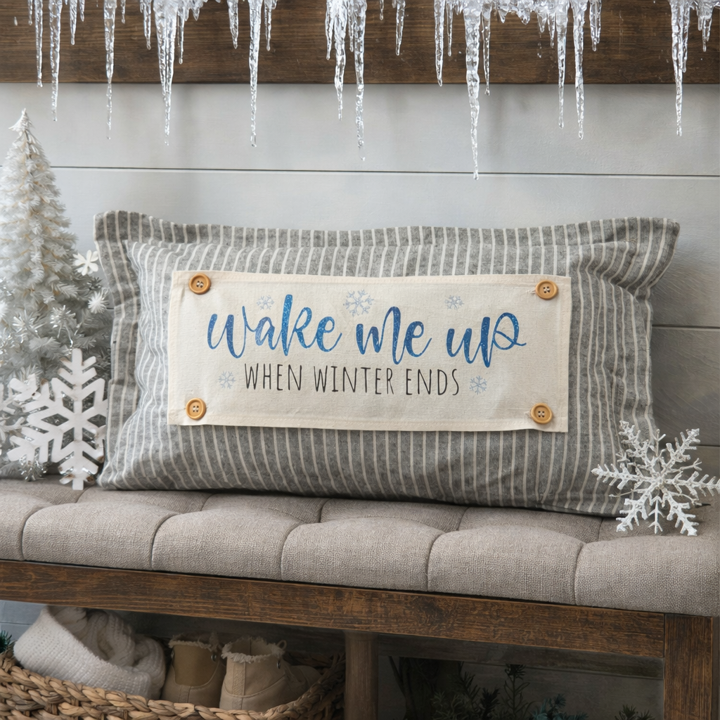 Decorative pillow with 'Wake me up when winter ends' text on a bench with winter decorations.