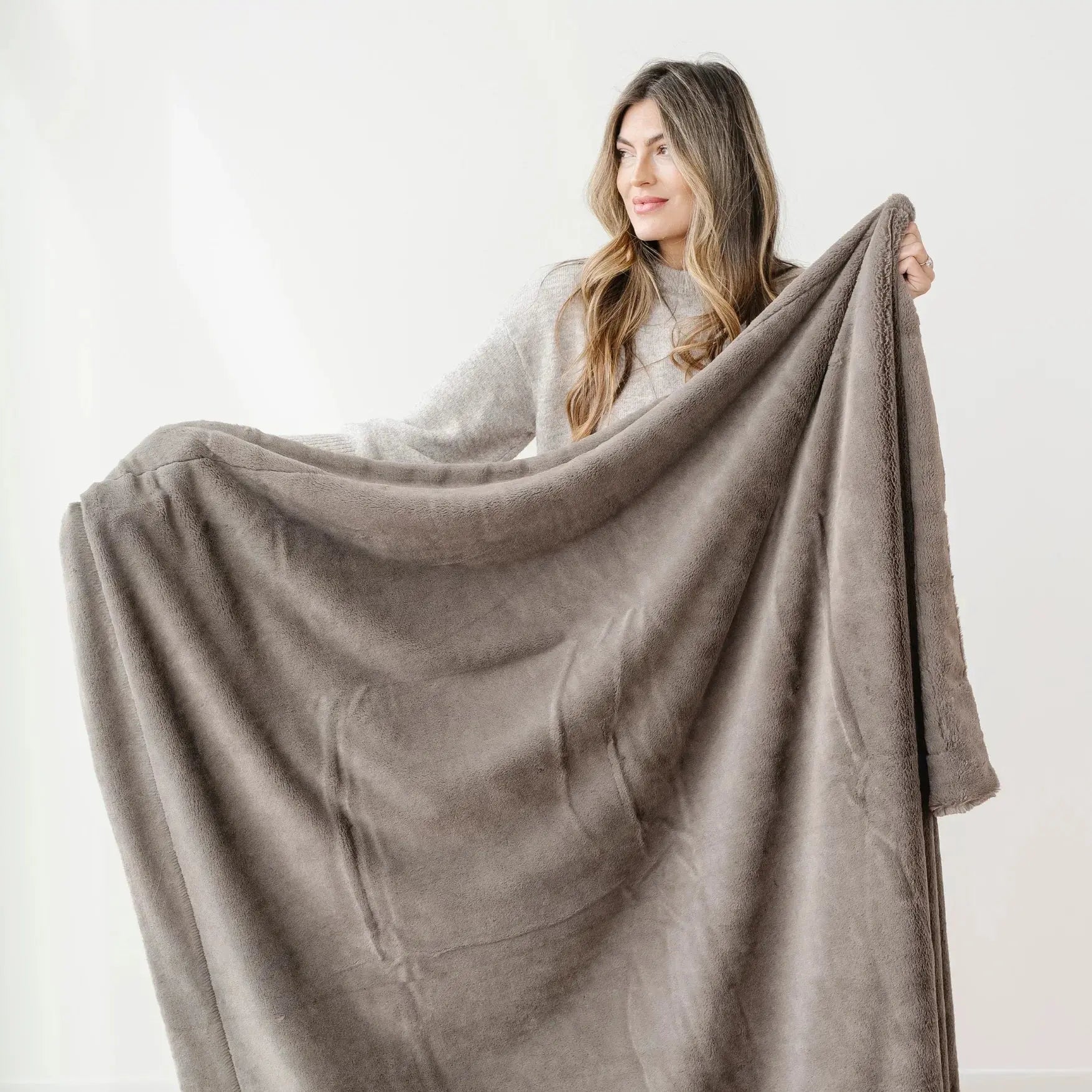 Woman holding a large beige blanket against a white background
