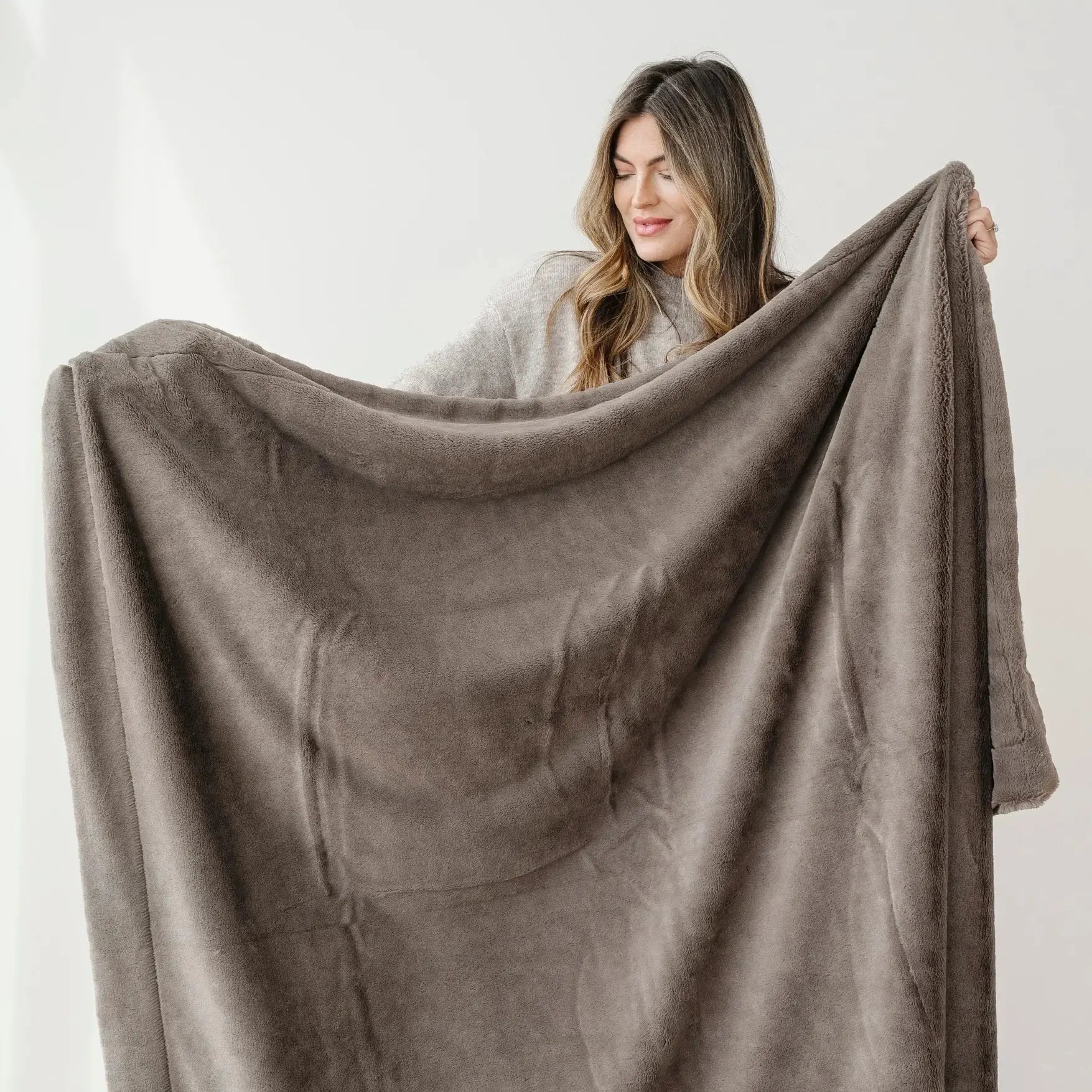 Woman holding a large brown blanket against a white background