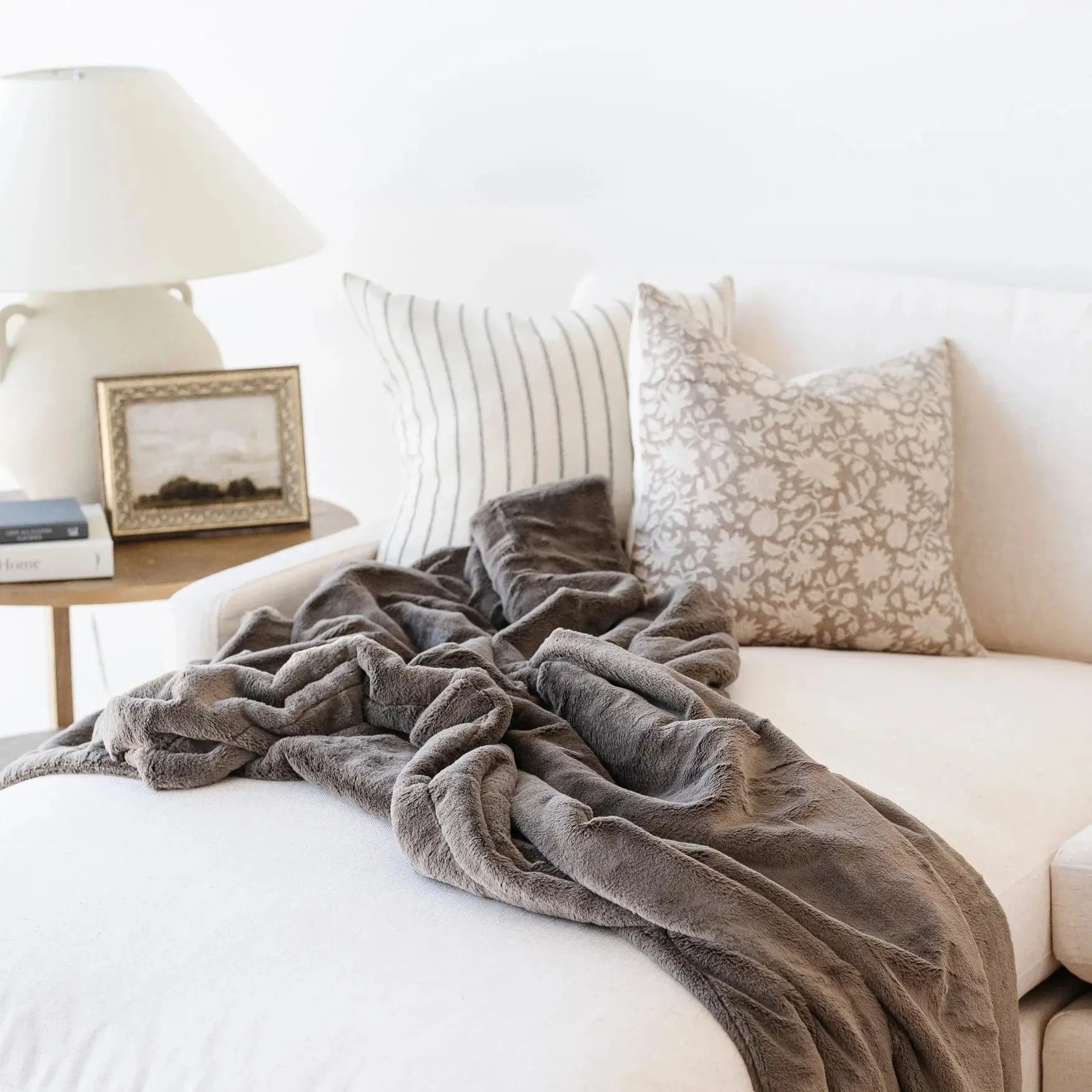 Gray blanket draped over a white sofa with decorative pillows in a cozy living room.