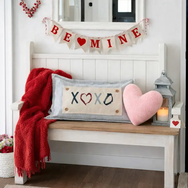 Decorative bench with heart pillow, red blanket, and 'Be Mine' banner in a home setting.
