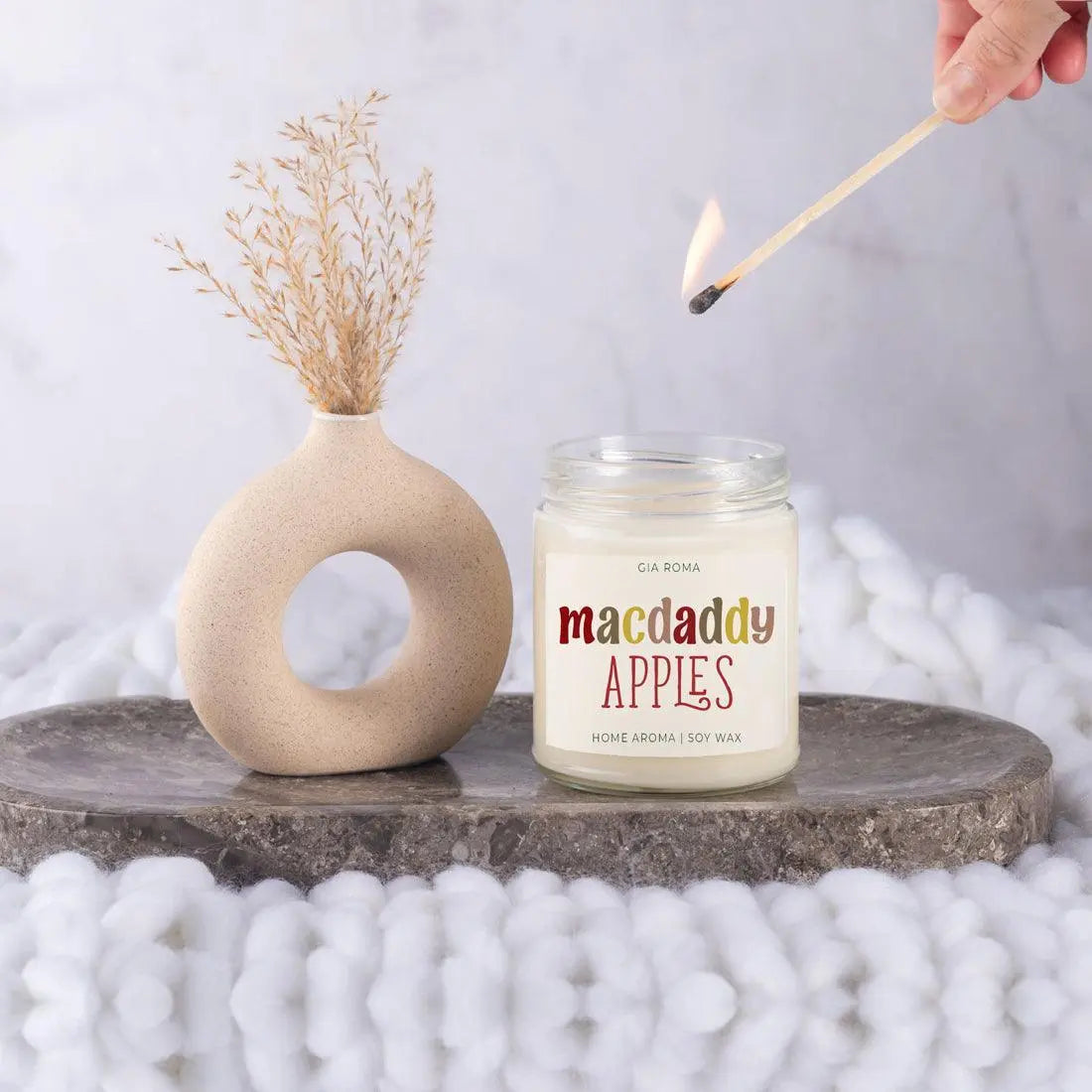 Candle labeled 'macdaddy APPLES' being lit with a decorative vase and white beads in the background.