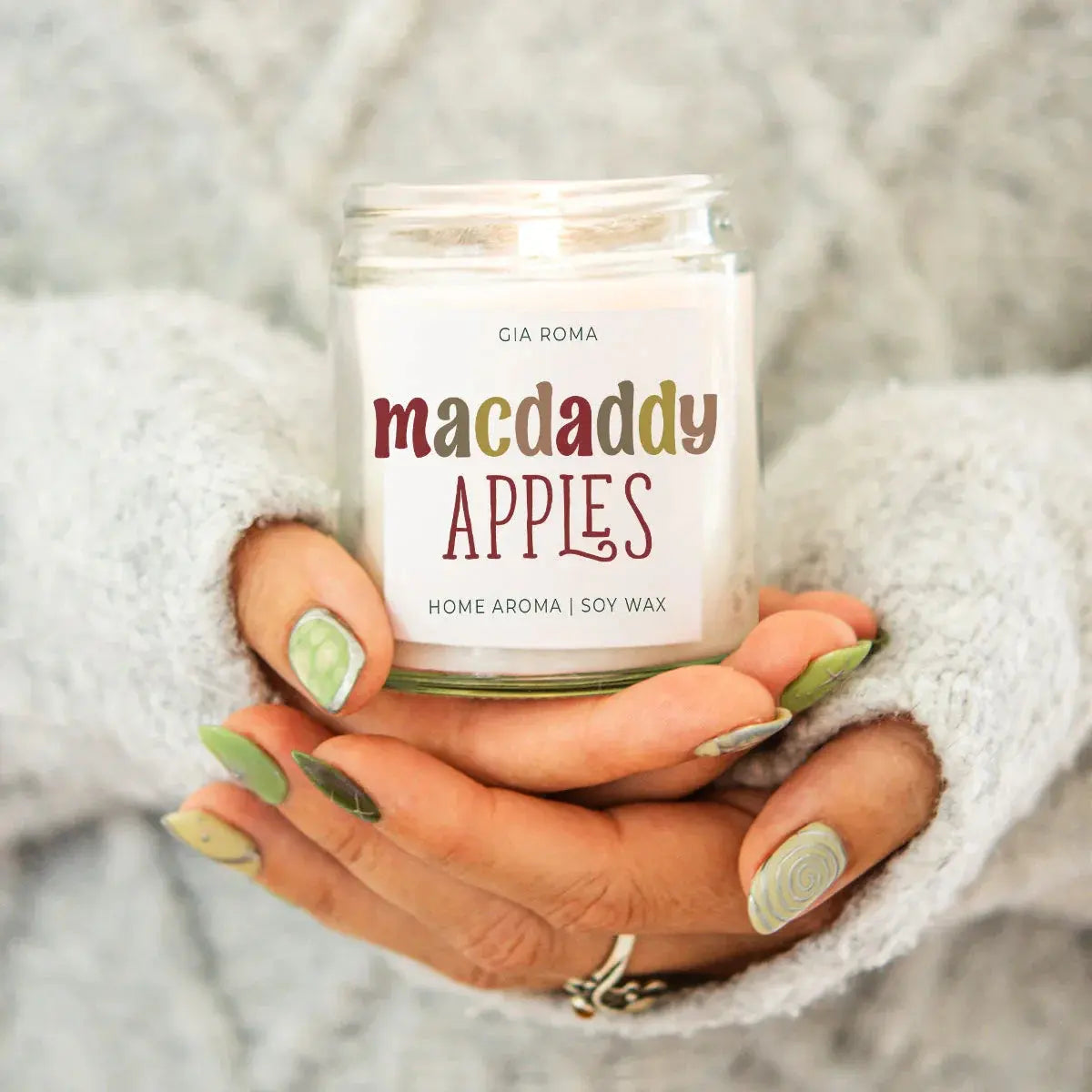 Candle labeled 'macdaddy APPLES' held by a person with green nail polish.