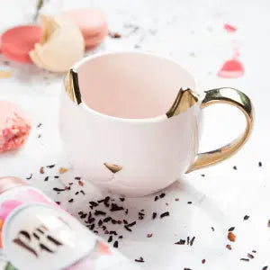 Decorative mug with gold accents on a surface with sprinkles and a pink flower.