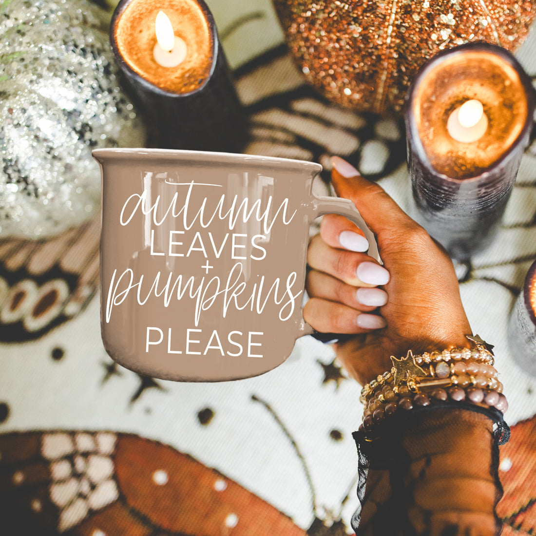 Hand holding a mug with 'autumn leaves + pumpkins please' text, surrounded by candles and autumn-themed decor.