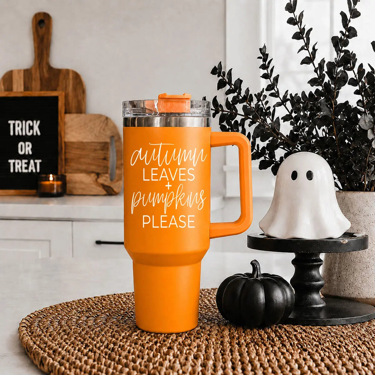 Orange travel mug with text in a kitchen setting with Halloween decorations.