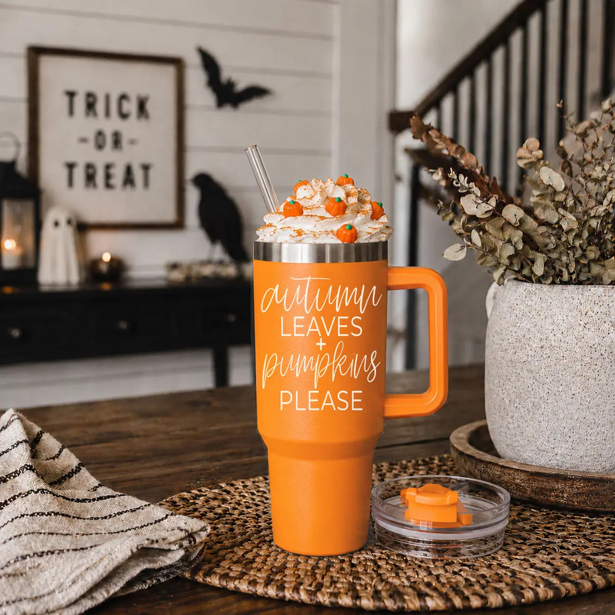 Orange mug with 'focus pocus I need coffee to focus' text, topped with whipped cream and candy corn, in a Halloween-themed room.