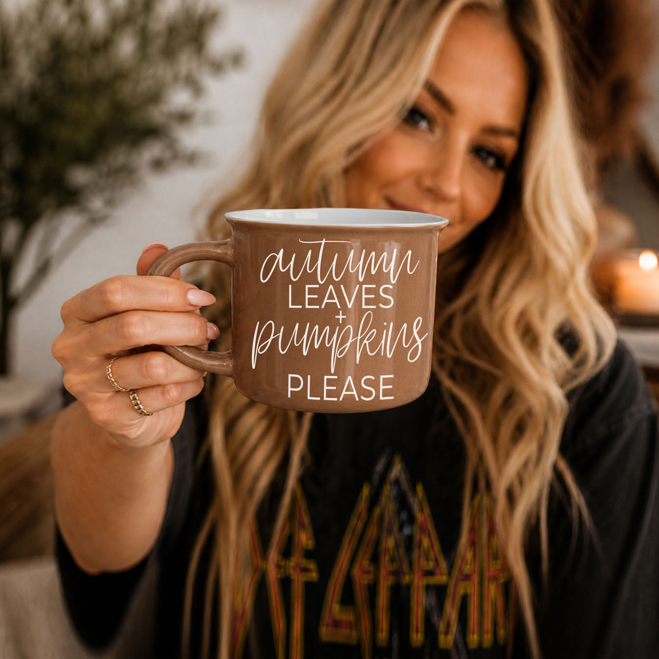 Woman holding a 'hello Fall' mug outdoors with blurred background