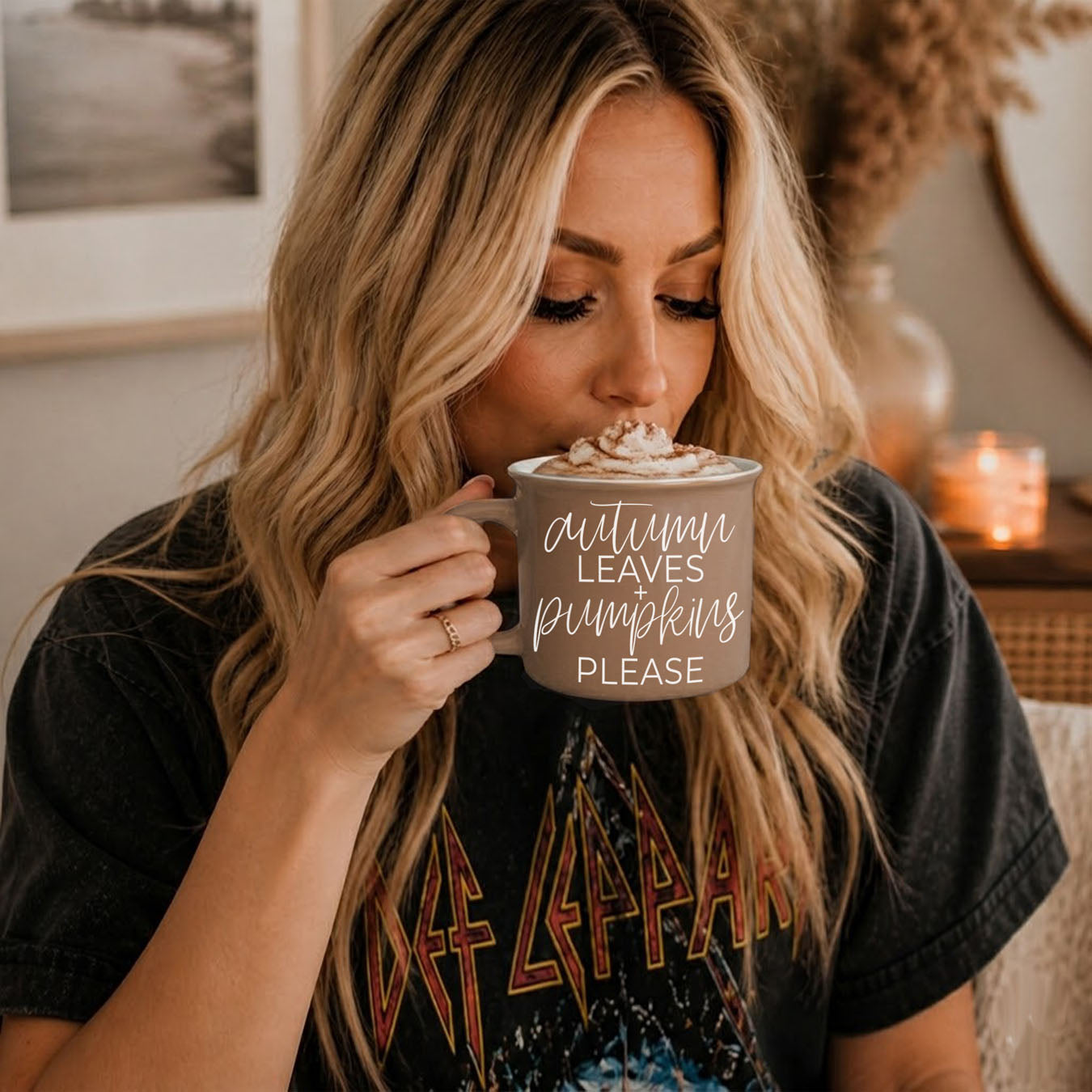 Woman drinking from a mug with 'autumn leaves pumpkins please' text in a cozy indoor setting.