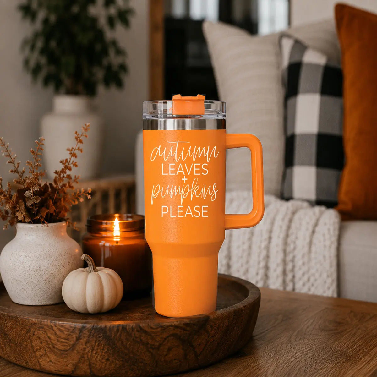 Orange travel mug with text on a wooden table in a cozy living room setting.