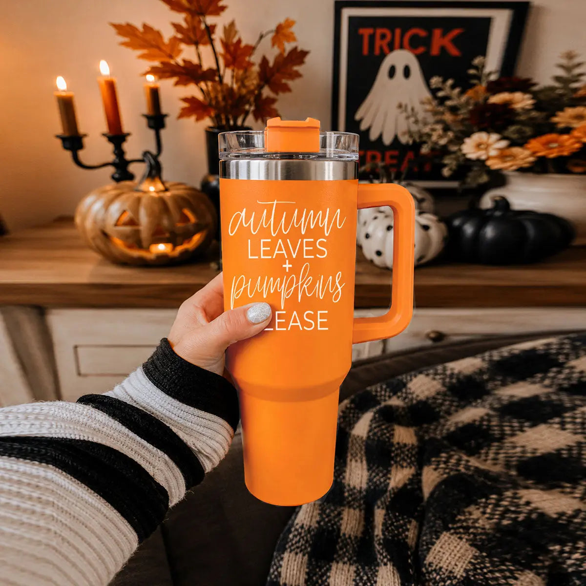 Person holding an orange tumbler with Halloween-themed text in a cozy indoor setting.