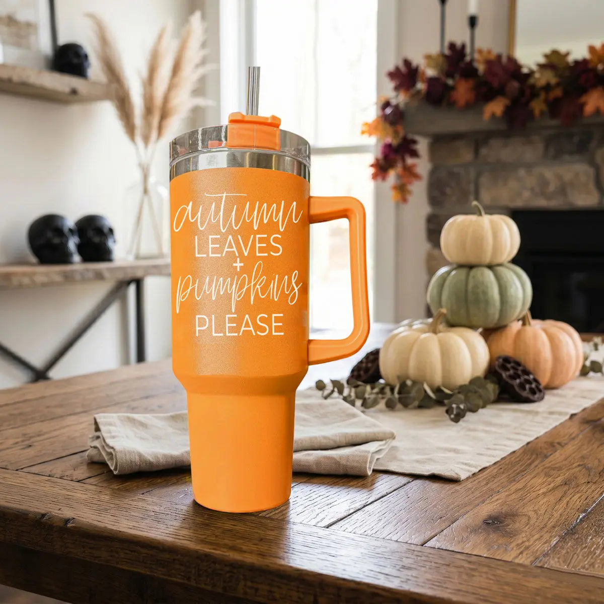 Orange mug with 'Autumn Leaves + Pumpkins Please' text on a wooden table with pumpkins in the background.