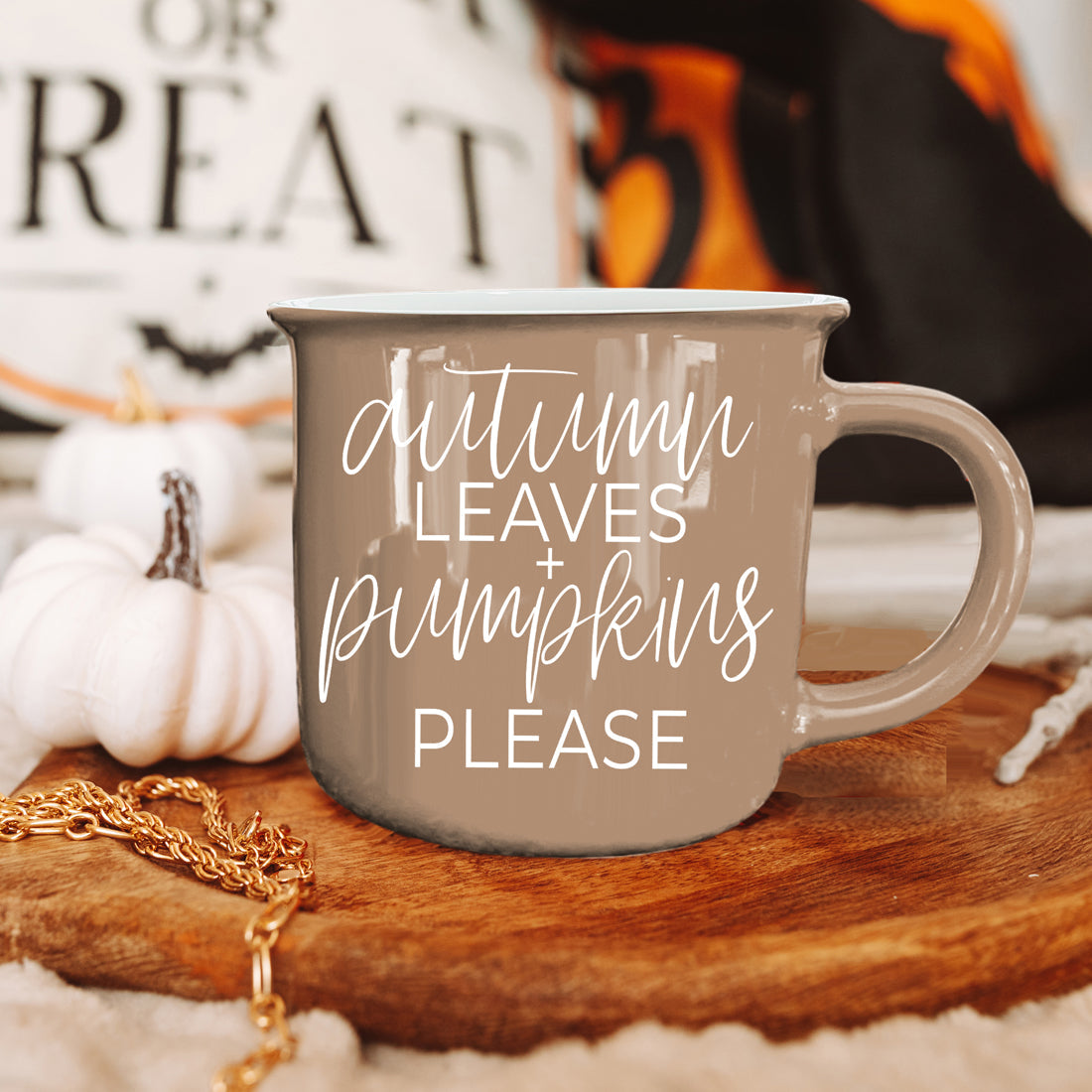 Mug with 'Autumn leaves + pumpkins please' text on a wooden surface with pumpkins and a blurred background.