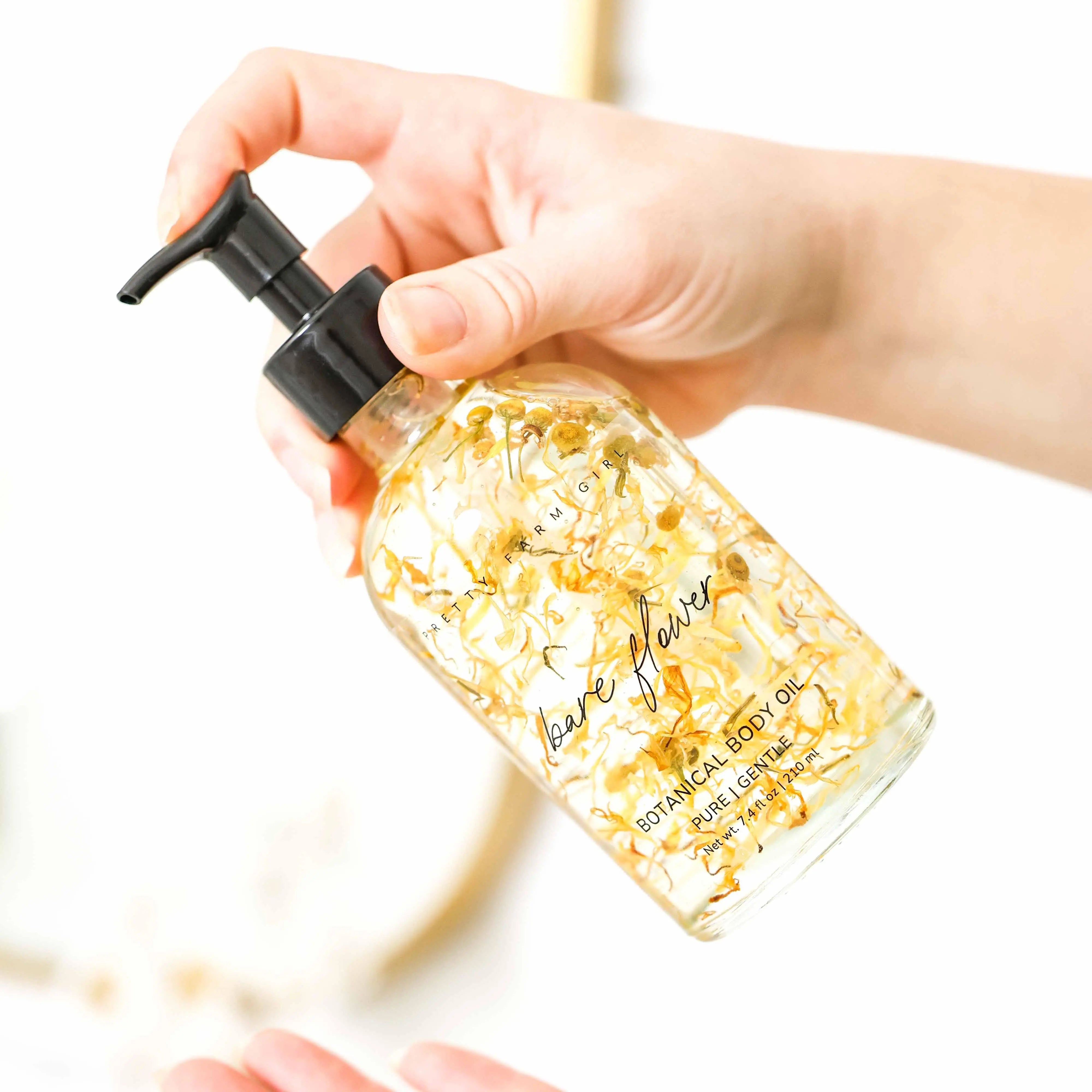 Hand holding botanical body oil with dried flowers, labeled 'bare flower' for gentle skin care