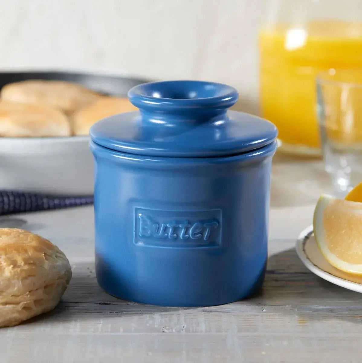 Blue ceramic butter crock with embossed label, farmhouse kitchen decor with biscuits and orange juice
