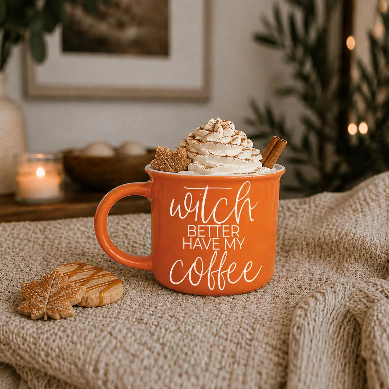 Orange mug with whipped cream, cookies, and a cinnamon stick on a textured surface.