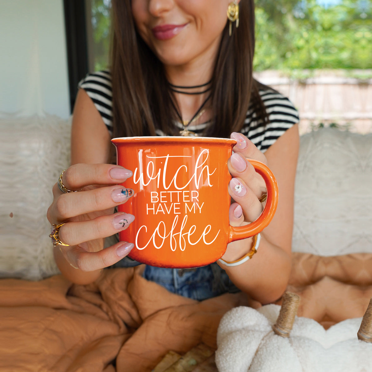 Woman holding an orange mug with text, sitting on a couch outdoors.