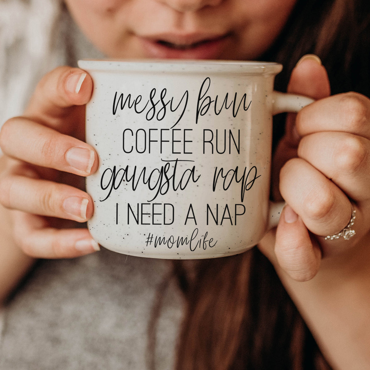 Person holding a mug with text 'messy bun coffee run gangsta rap I need a nap #momlife'