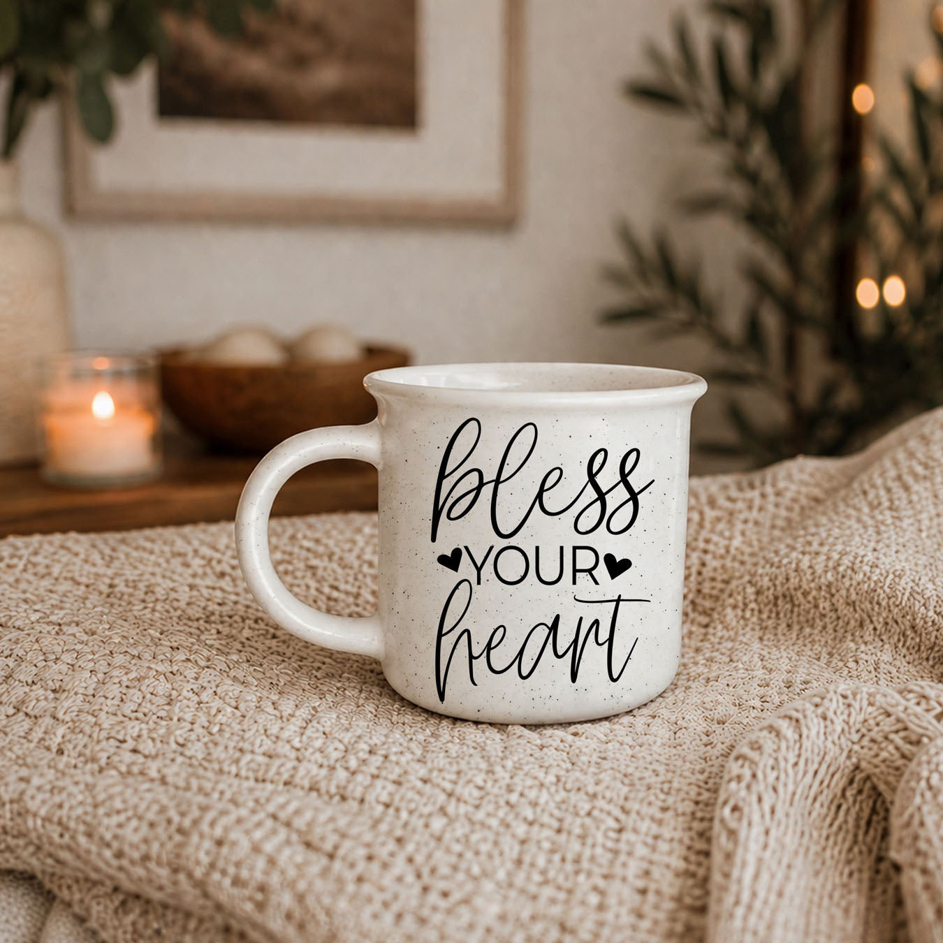 White mug with 'bless your heart' text on a textured surface with candles and plants in the background