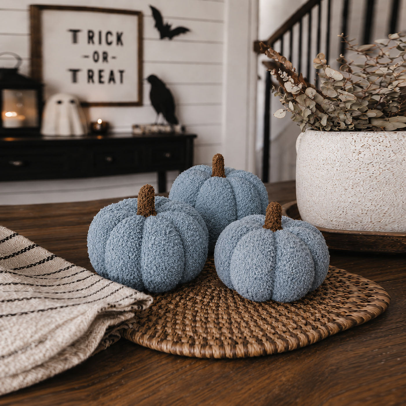 Blue textured pumpkins on a woven mat with Halloween decorations in the background.