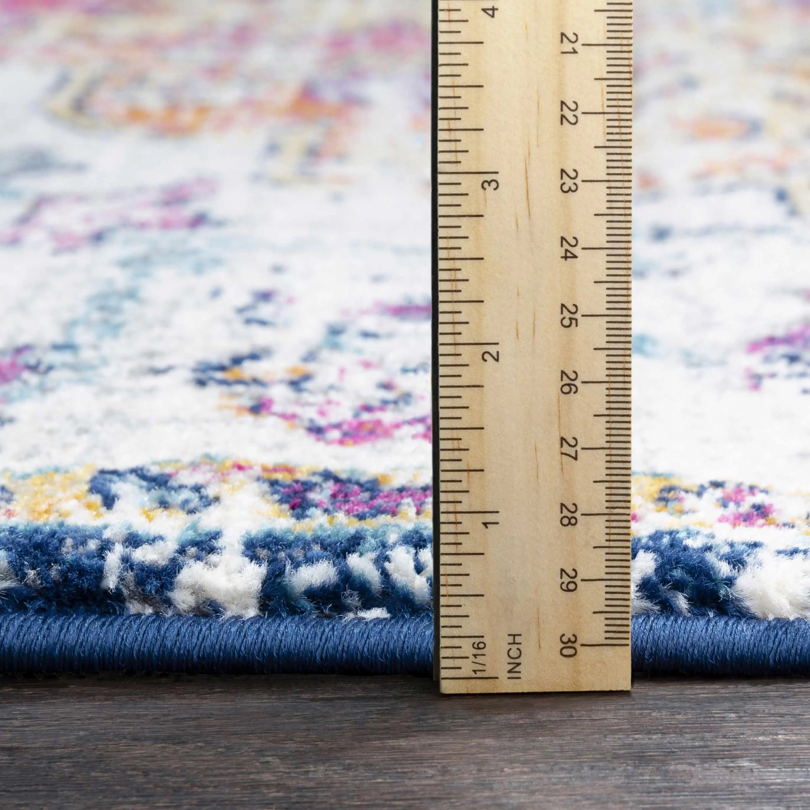 Colorful boho rug with blue border, measuring pile height with wooden ruler for farmhouse decor