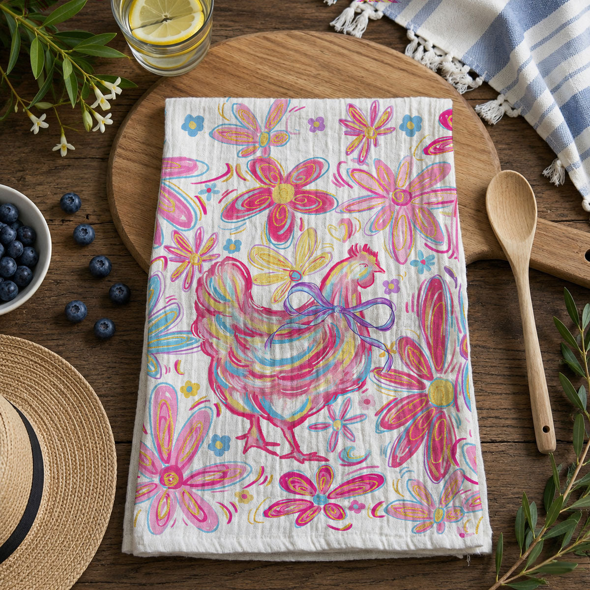Colorful towel with a rooster design on a wooden table with blueberries and a straw hat.