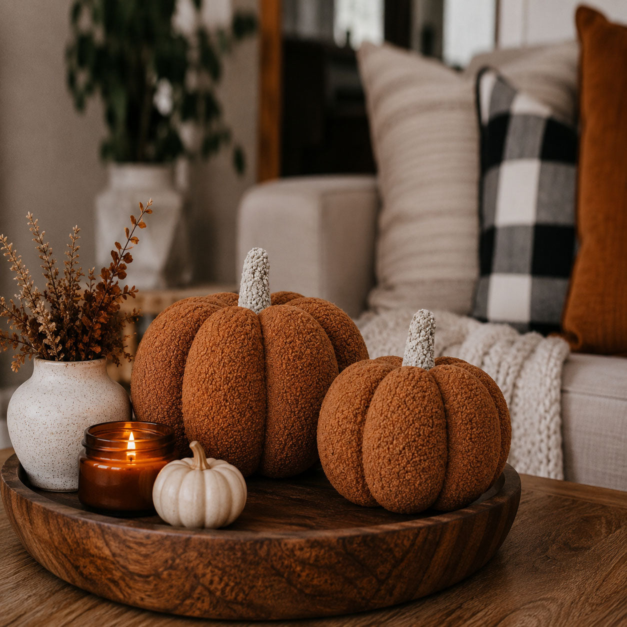 Decorative pumpkins on a wooden tray with a candle and plant in a cozy living room setting.