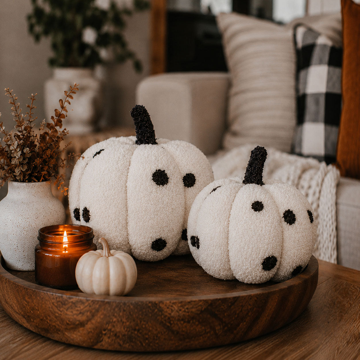 Decorative pumpkins on a wooden tray with a candle and small white pumpkin in a cozy living room setting.