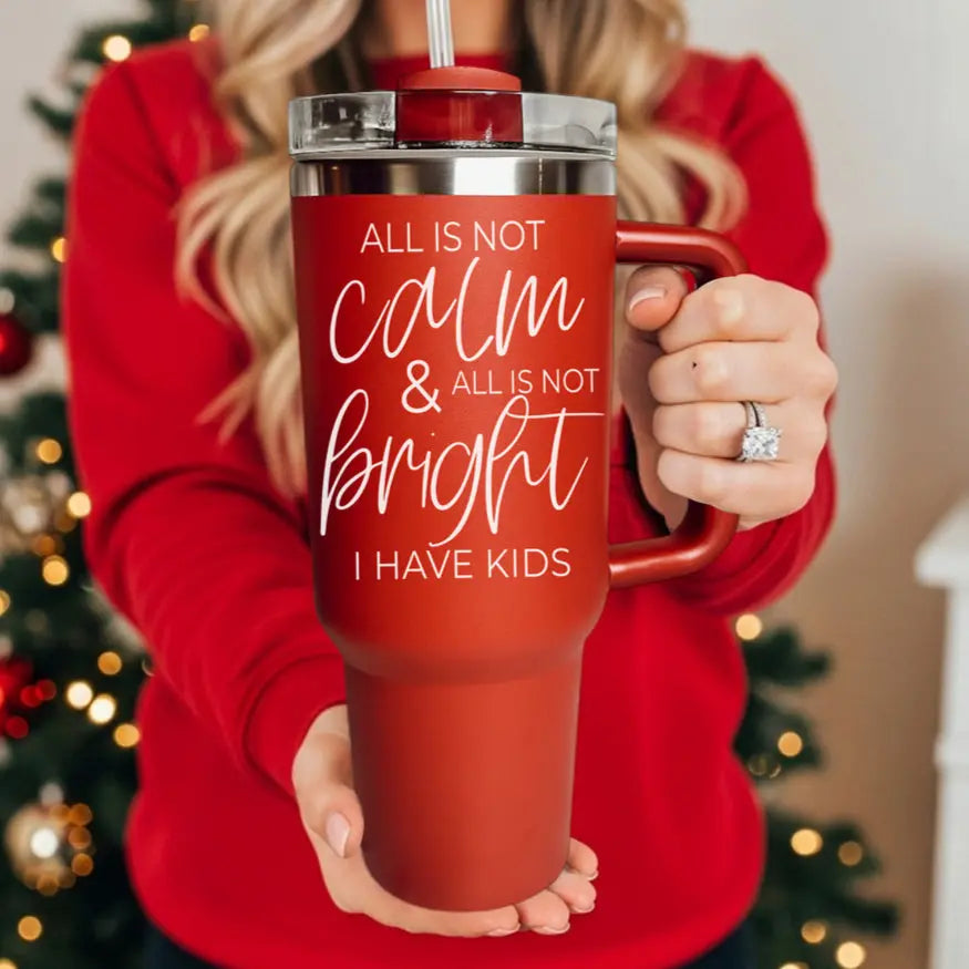 Person holding a red tumbler with text in front of a Christmas tree