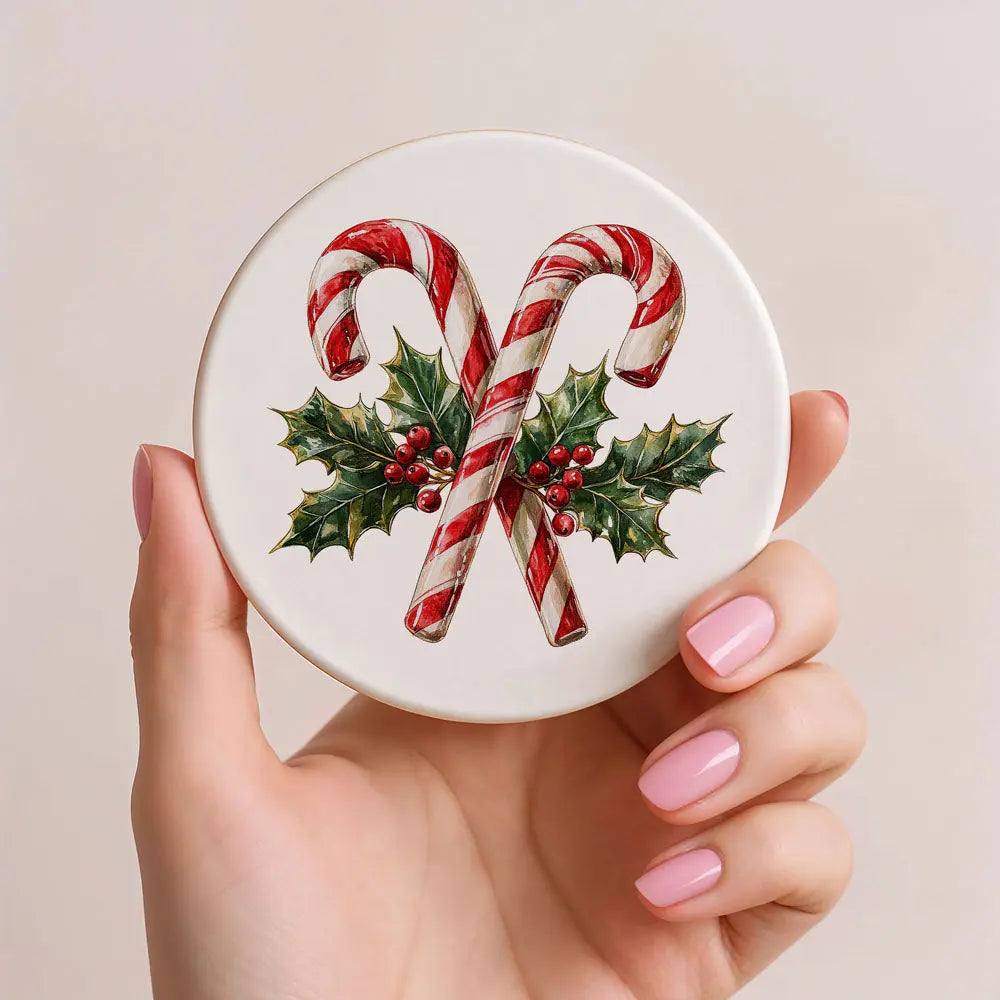 Round white object with candy canes and holly leaves held by a hand with pink nail polish.