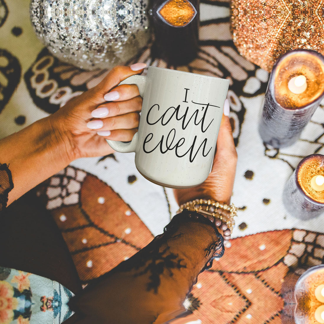 Person holding a mug with 'I can't even' text on a decorative surface with candles.
