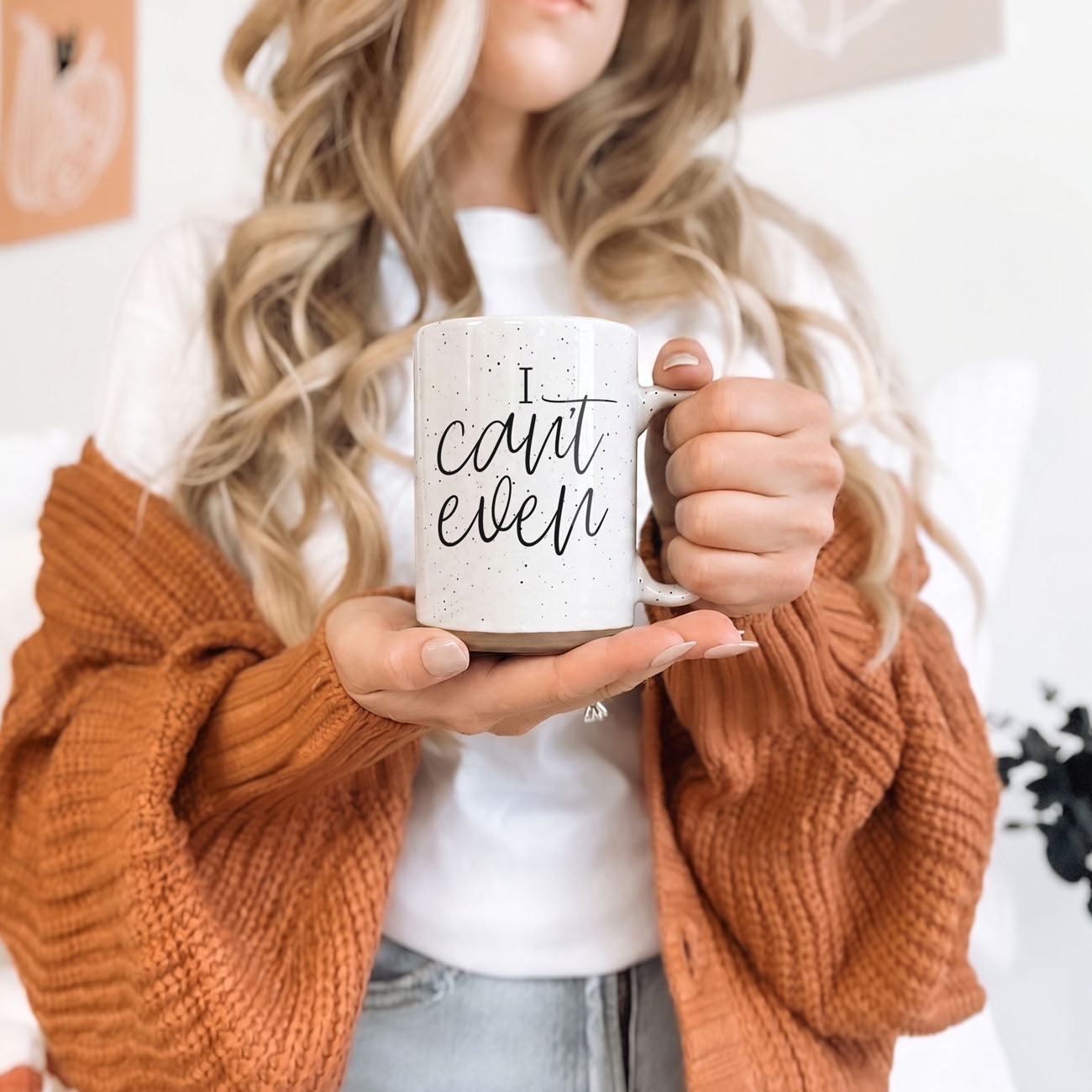 Person holding a mug with text, wearing an orange sweater.