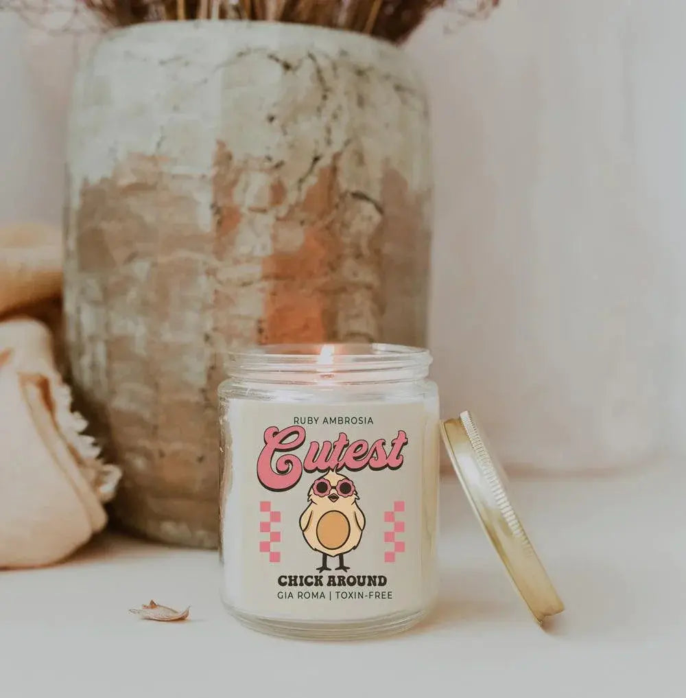 Candle in a jar with a cute design and text, placed on a surface with a blurred background.