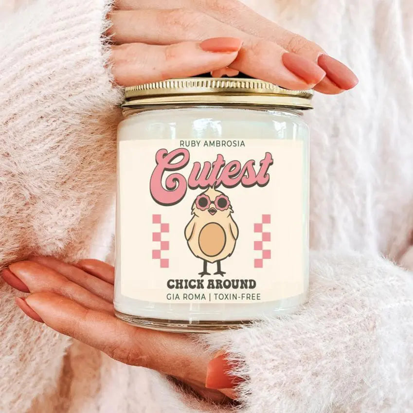 Candle jar labeled 'Cutest Chick Around' held by a person with pink nail polish against a soft pink background.