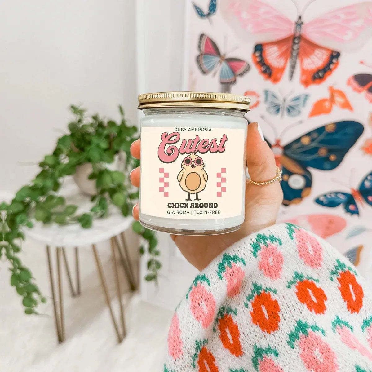 Hand holding a candle labeled 'Cutest Chick Around' with a colorful butterfly design in the background