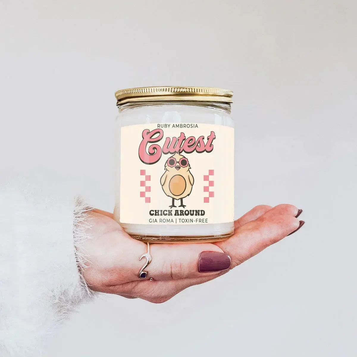 Candle with a cute label featuring a chick design held in a hand against a light background